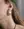 Close-up of a woman's ear wearing WALD Berlin's Pop Soleil Earrings—large, 18k gold plated sunburst design with wax pearl accents. She also wears two small studs in her upper ear and part of a beaded necklace is visible.