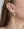 Close-up of a person's ear wearing WALD Berlin's Pop Wave Earrings Big, thick gold-plated brass spirals; brown hair and part of a gold necklace are also visible.