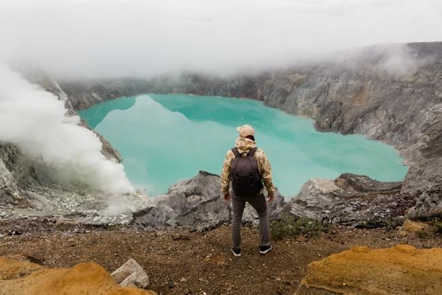 Man tourist looks at the sulphur lake on the Ijen volcano on the island Java in Indonesia. Hiker man with backpack travel on top mountain, travel concept