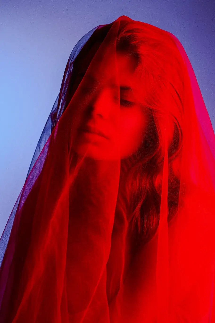 Portrait of a woman shrouded in a red veil with a contrasting blue background.
