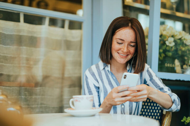 Jovem mulher mexendo no celular, feliz por ter recebido voucher de desconto.