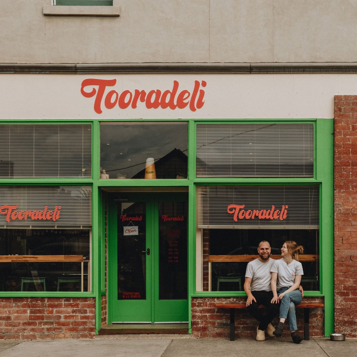Two people sitting outside the green Tooradeli storefront