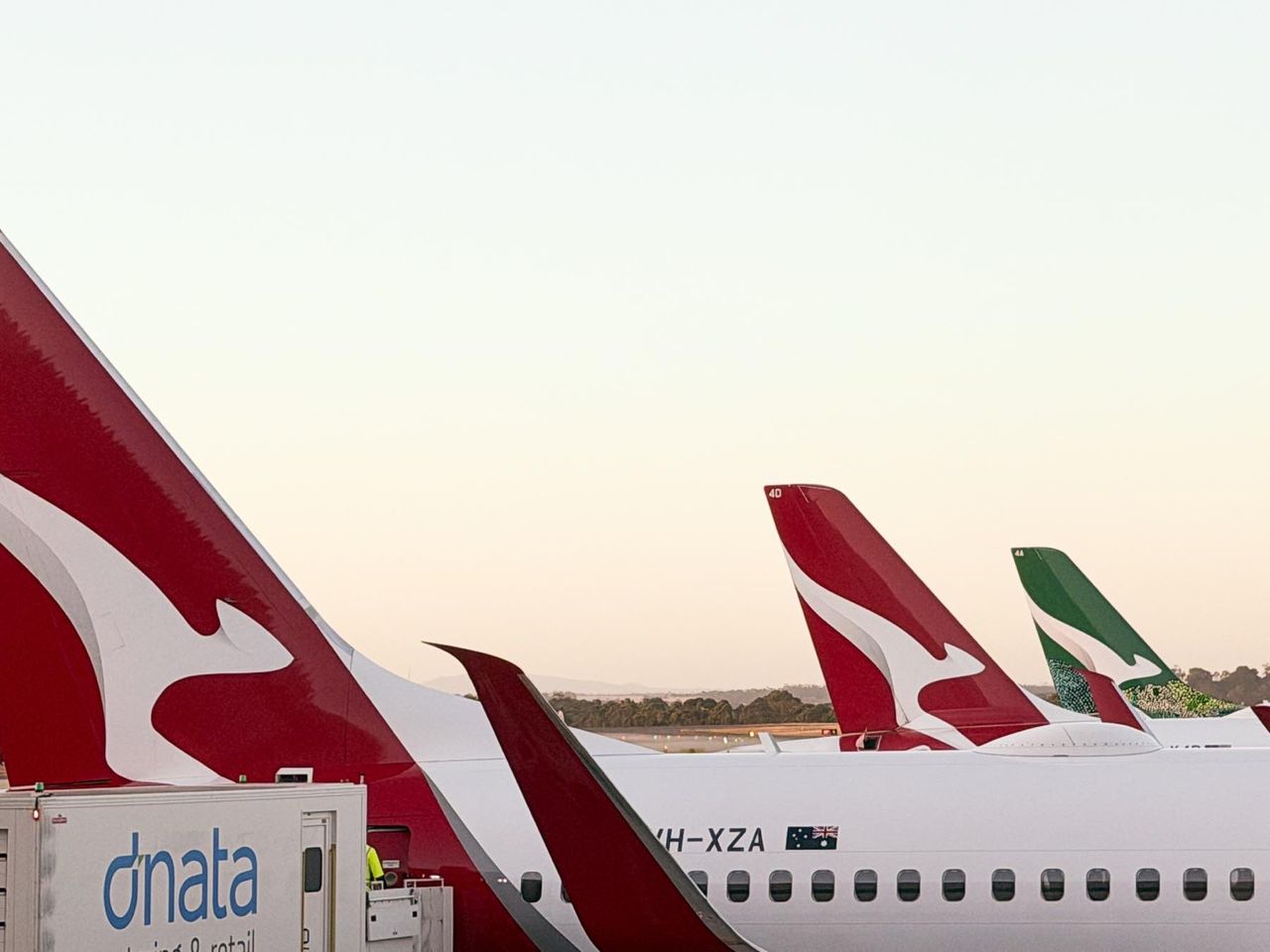 Airplanes with red and white tails parked at an airport under a clear sky.