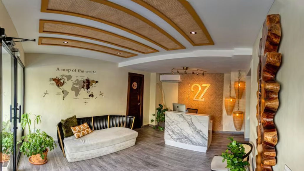 Lobby moderno y elegante del Studio 27 Hotel en Santo Domingo, que muestra un mostrador de recepción de mármol con el logotipo del número 27 iluminado, un sofá contemporáneo, plantas de interior y un mapa del mundo decorativo en la pared.