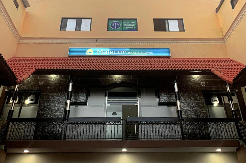 Facade of Malecon Rooms & Hotel in Santo Domingo featuring its illuminated main sign and a rustic-style balcony.