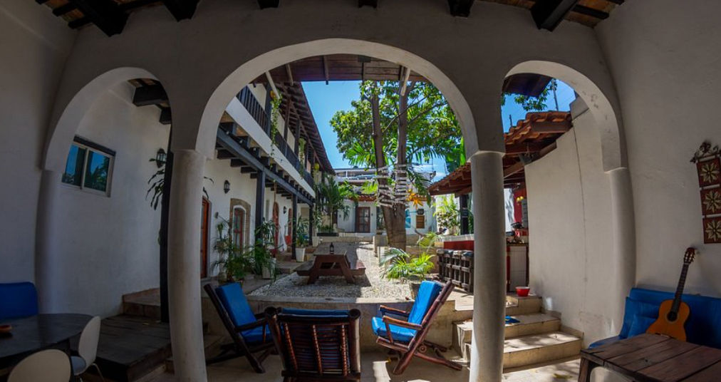 Patio interior colonial con piscina pequeña, hamaca, árboles y balcones de madera en un hostal de Santo Domingo