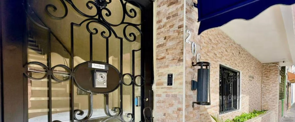 Entrance facade of Tau Casa Santomé featuring a black wrought iron gate, doorbell intercom, and the number 206 on the stone wall