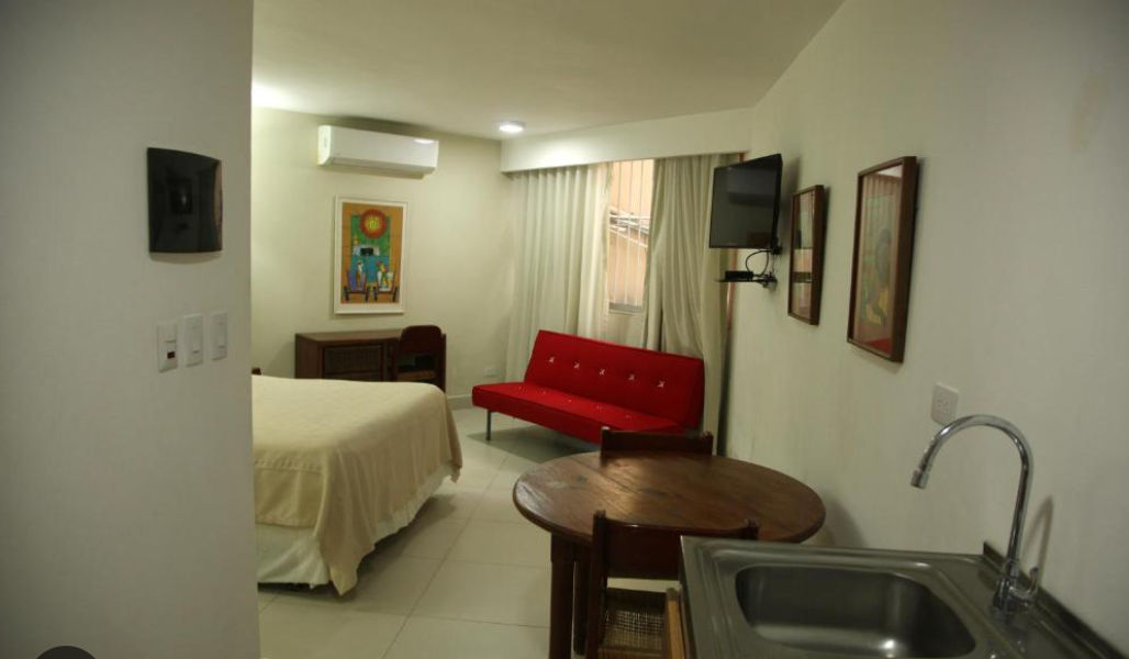 Reception desk at Aparta Hotel Plaza del Sol featuring a wooden counter, a white sofa, air conditioning, and the hotel name on the back wall.