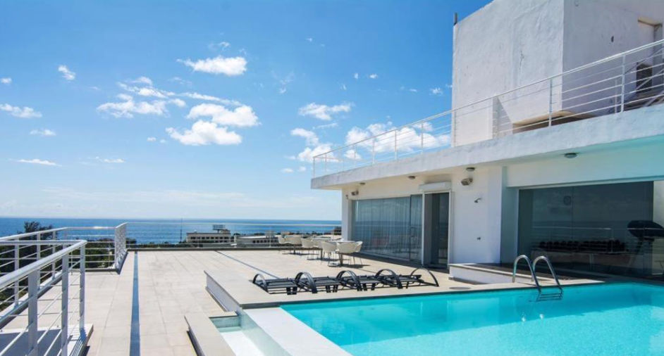 Rooftop terrace featuring a swimming pool, lounge chairs, and dining tables with ocean views under a clear blue sky.