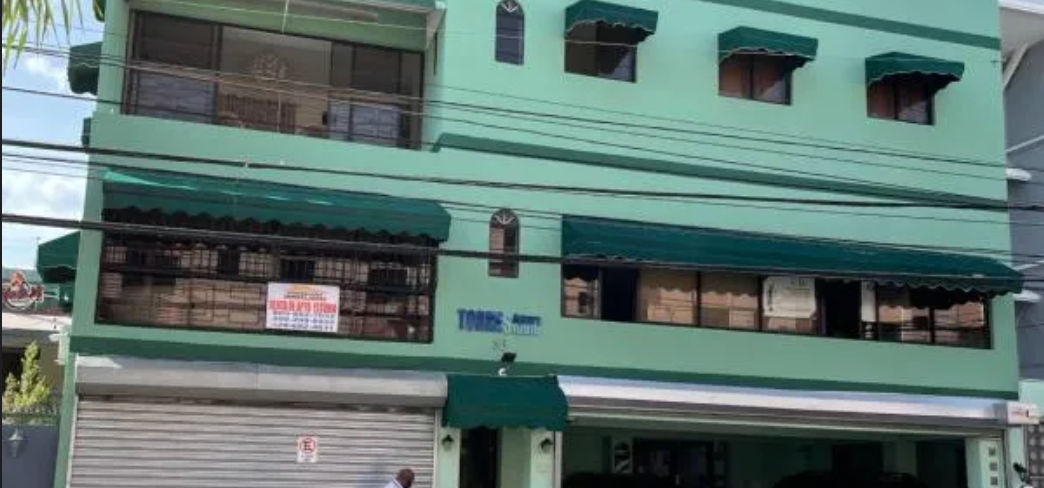 Fachada del hotel Torres Apart Studio, un edificio verde de tres pisos con toldos oscuros en las ventanas en Santo Domingo, República Dominicana.