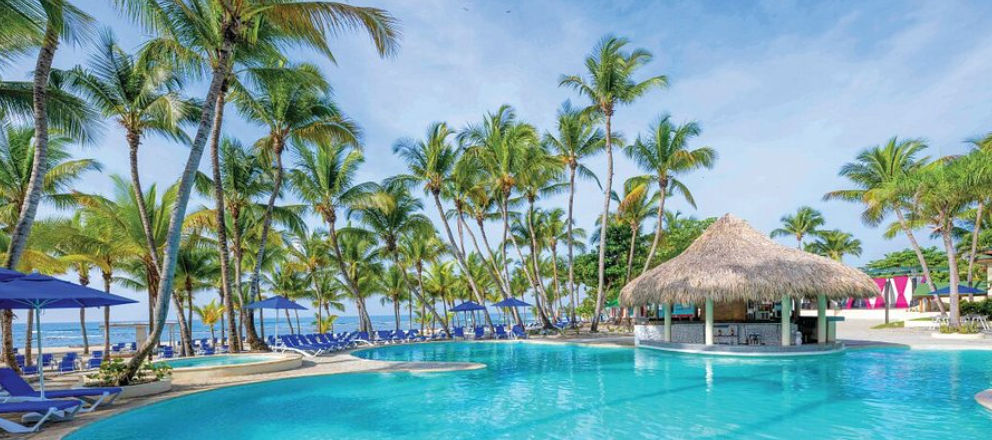 Outdoor swimming pool surrounded by palm trees with a thatched-roof palapa bar at the beachfront Coral Costa Caribe hotel