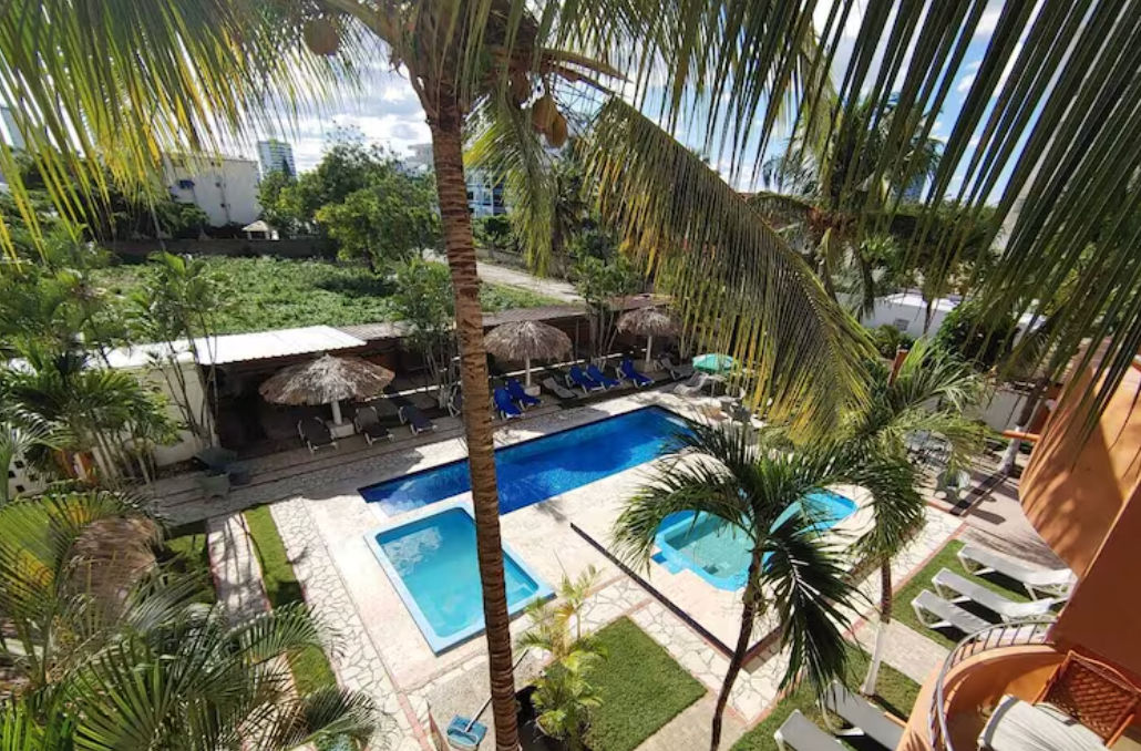 Fachada del hotel Meridian Residence Juan Dolio con balcones naranjas y palmeras bajo un cielo parcialmente nublado en la República Dominicana
