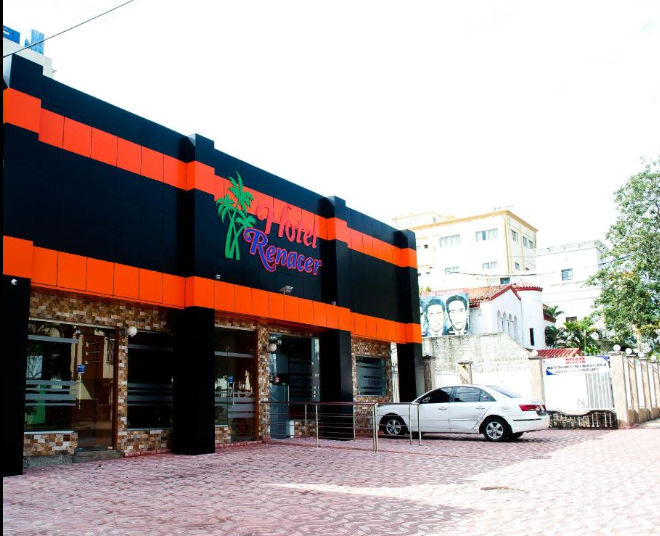 Fachada exterior del Hotel Renacer con diseño en negro y naranja y un automóvil blanco estacionado al frente.