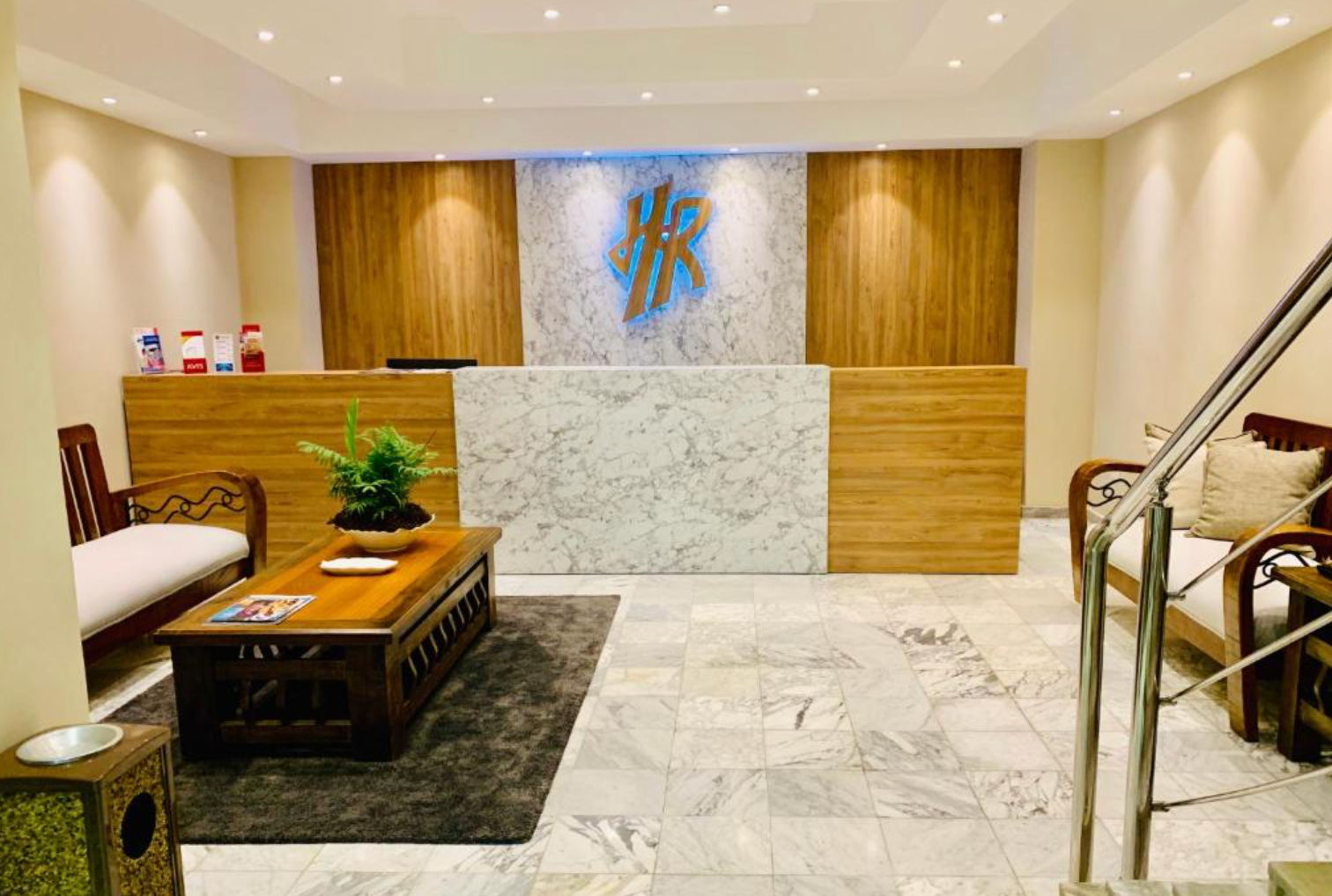 Lobby y área de recepción del Hotel Riazor con pisos de mármol, mostradores de madera y el logotipo HR iluminado en la pared trasera.