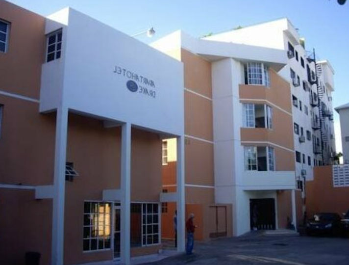 Fachada exterior del Aparta Hotel Drake Piantini en Santo Domingo, mostrando la entrada principal del edificio en tonos beige y blanco con su letrero informativo.