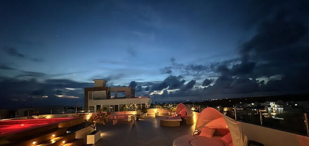 Rooftop terrace at All Seasons Hotel Bayahibe at night featuring an illuminated pool and canopied sunbeds