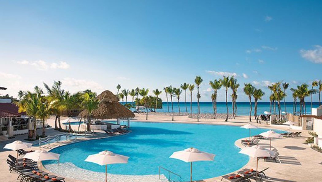 Piscina principal al aire libre con camastros, sombrillas blancas y bar de palapa frente a la playa tropical en Dreams Dominicus La Romana