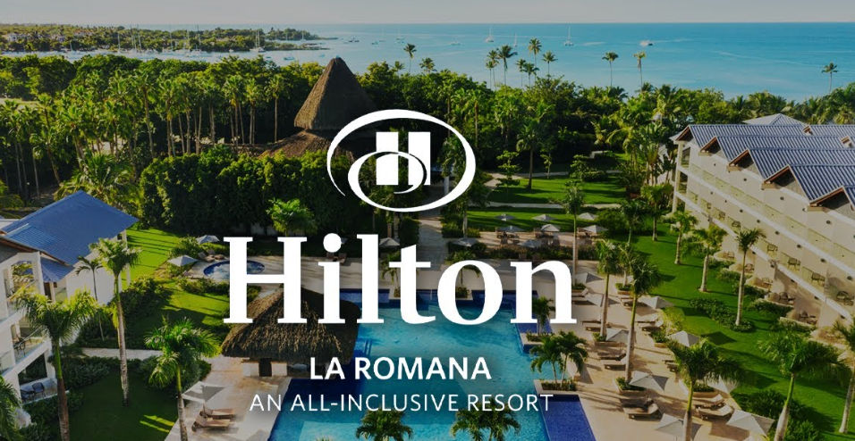 Vista aérea del Hilton La Romana An All-Inclusive Resort con piscina tropical, palmeras y el mar Caribe de fondo.