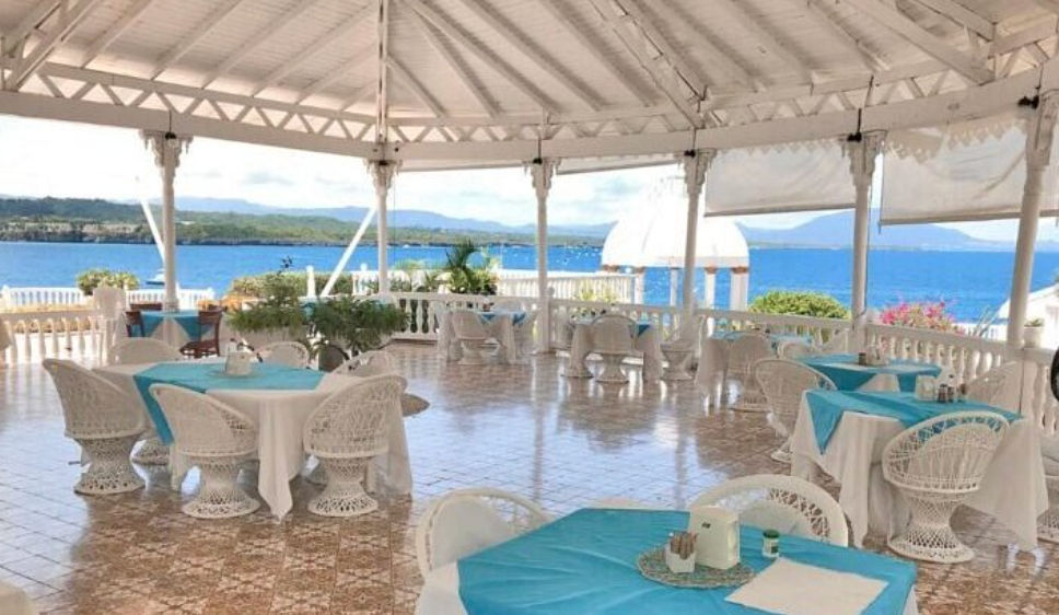 Vista aérea del Piergiorgio Palace Hotel en Sosúa, mostrando su arquitectura victoriana blanca sobre un acantilado frente al mar caribeño y una pequeña playa privada