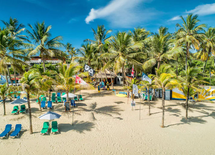 Fachada blanca del Hotel Villa Taina en Cabarete con balcones arqueados, palmeras y sombrillas tropicales frente a la piscina