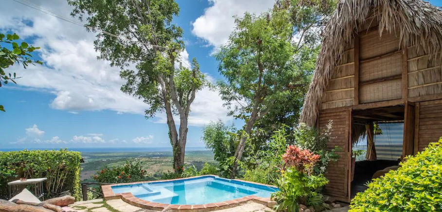 A rustic wooden cabin with a thatched roof overlooking a small plunge pool and a stunning view of the coastline in Tubagua.