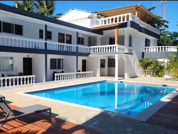 Fachada exterior blanca de The Hummingbird Cabarete con balcones, plantas tropicales y palmeras bajo un cielo despejado