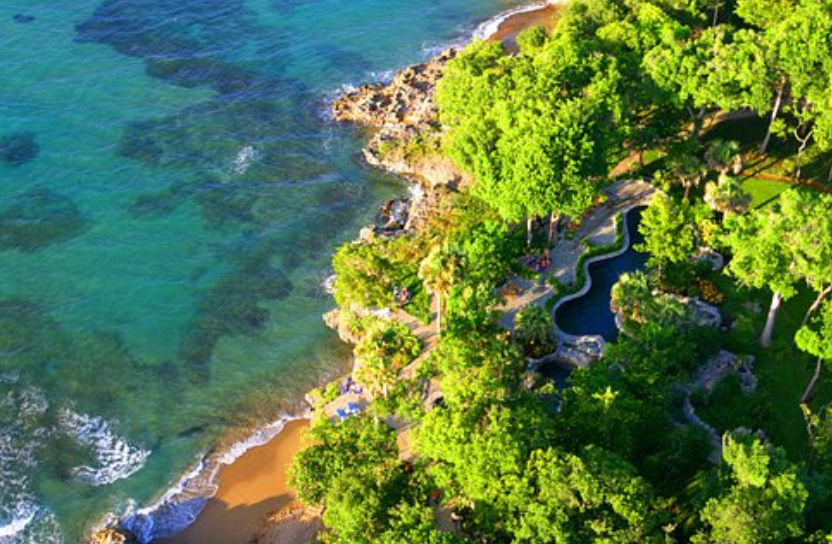 Aerial view of a luxury villa featuring brown tiled roofs, an integrated private pool, and tropical gardens