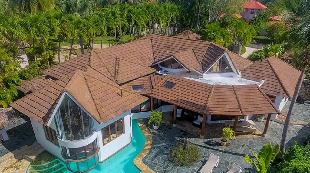 Vista aérea de una villa de lujo con techos de tejas marrones, piscina privada integrada y jardines tropicales.