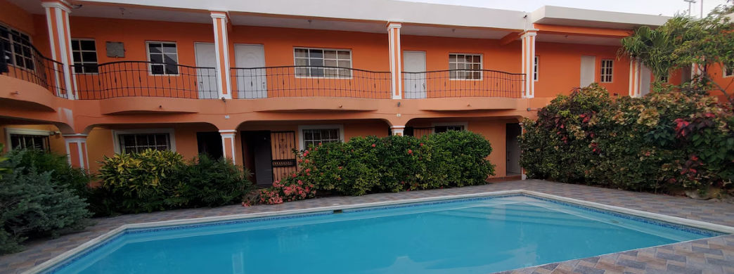 Fachada del Apartahotel Next Nivel en Punta Cana con su piscina al aire libre, balcones y paredes de color naranja tropical.