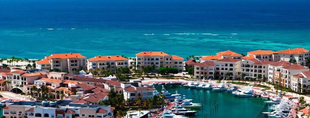Aerial view of luxury boats and yachts docked at the Cap Cana marina, surrounded by residential buildings with red-tiled roofs and the Caribbean Sea in the background in Punta Cana, Dominican Republic.