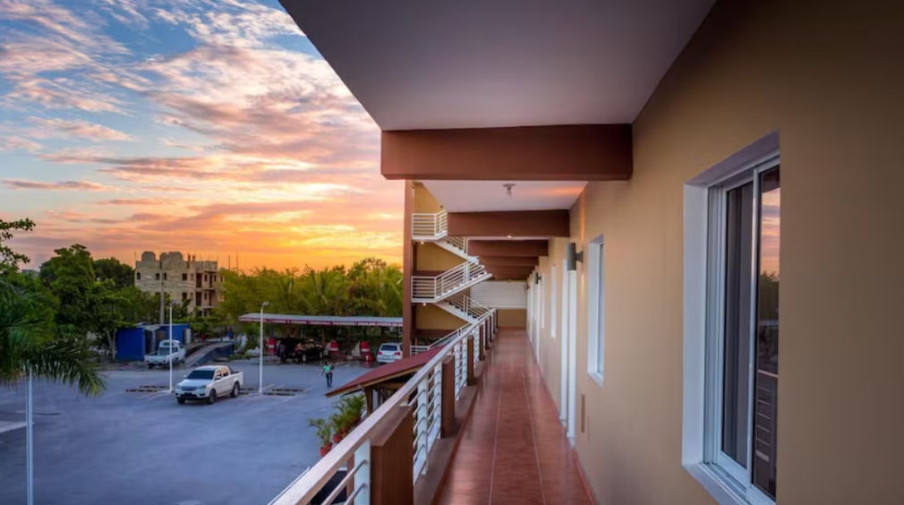 Exterior facade of My Home Hotel Punta Cana at dusk, a three-story brown building featuring white balconies, a parking area, and ground-floor commercial spaces.