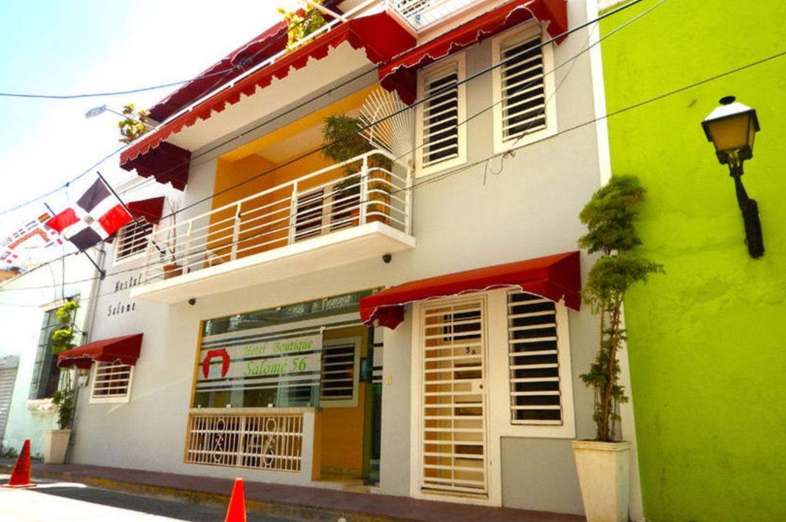 Exterior facade of Hotel Boutique Salomé 56 featuring red awnings, a white balcony, and the Dominican Republic flag."