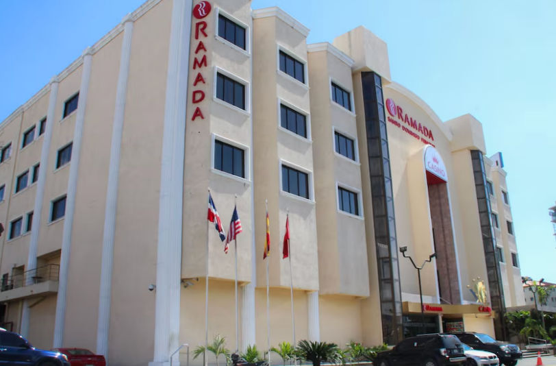 Fachada exterior del Ramada Santo Domingo Princess Hotel con banderas ondeando en la entrada y vehículos estacionados frente al casino.