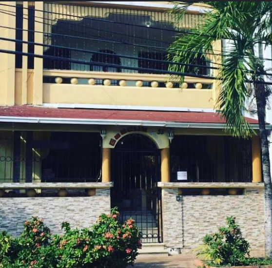 Fachada exterior del Caribbean Hotel Santo Domingo en el sector de Gascue, un edificio residencial de dos niveles de color amarillo con el número 53 y una entrada con rejas negras.