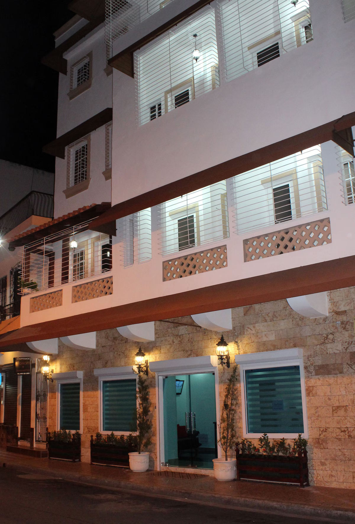 Fachada exterior nocturna del Hotel Merey en Santo Domingo, mostrando la entrada iluminada, paredes de piedra y balcones de estilo colonial con herrería.