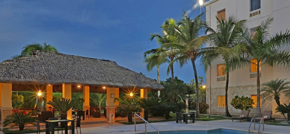 Área de la piscina del hotel Four Points by Sheraton en Punta Cana con un gazebo de techo de paja iluminado, palmeras y camastros al atardecer.