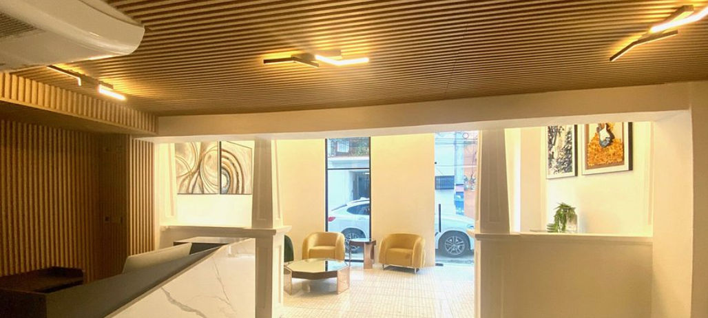 Lobby moderno y elegante del hotel RIG Colonial Experience en Santo Domingo, con paredes y techo de listones de madera, iluminación cálida, sillones amarillos y recepción de mármol blanco.