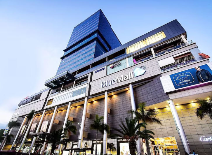 Exterior facade of BlueMall Santo Domingo featuring a large modern glass tower and luxury retail stores on the ground floor.