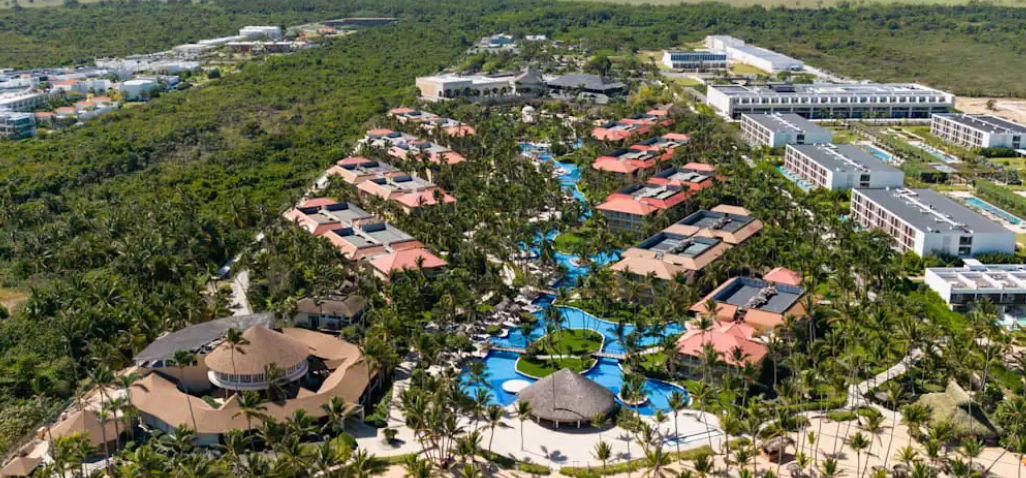 Aerial view of the Jewel Punta Cana Beach Resort showing its extensive winding pool, tropical gardens, yellow buildings, and the Caribbean Sea in the background.