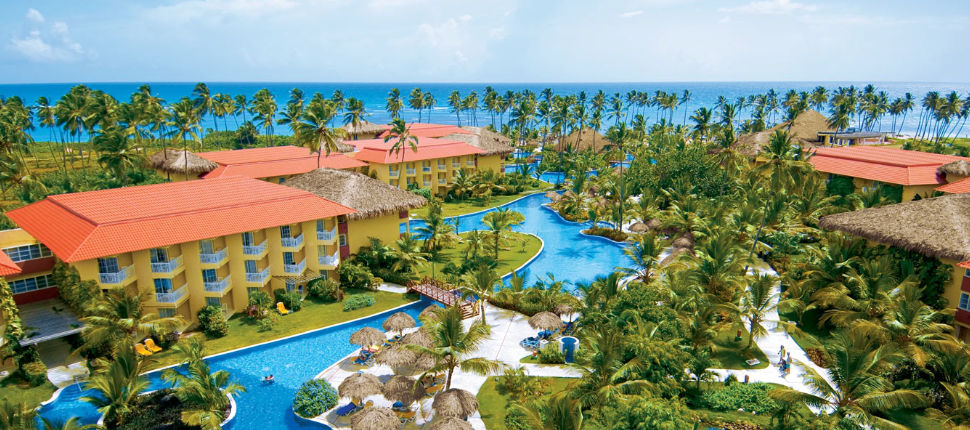 Vista aérea del Jewel Punta Cana Beach Resort mostrando su extensa piscina serpenteante, jardines tropicales, edificios amarillos y el mar Caribe al fondo.