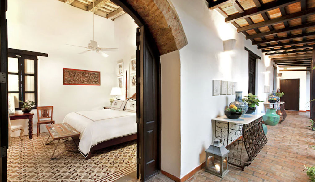 Interior courtyard at Casas del XVI featuring a swimming pool, lounge chairs, and a seating area surrounded by illuminated palm trees at dusk in Santo Domingo