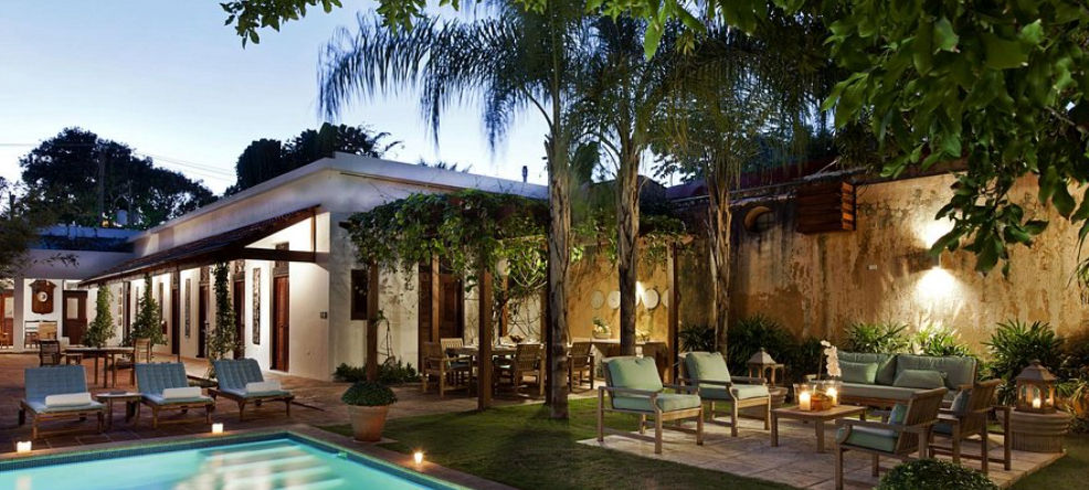 Interior courtyard at Casas del XVI featuring a swimming pool, lounge chairs, and a seating area surrounded by illuminated palm trees at dusk in Santo Domingo.