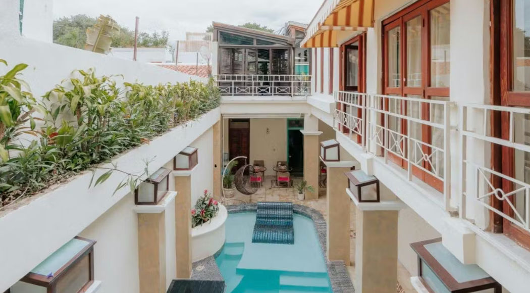 Interior courtyard of Casa Sanchez Hotel featuring a long swimming pool, colonial balconies, and exotic greenery