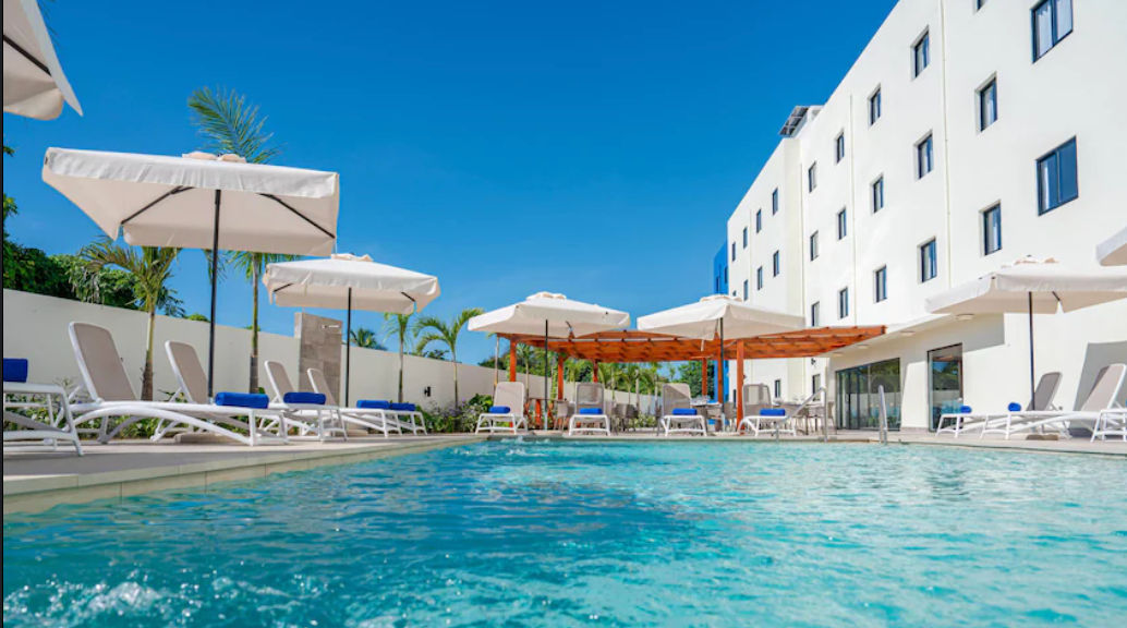 Piscina exterior del hotel Days Inn By Wyndham Juan Dolio rodeada de sillas de playa y palmeras