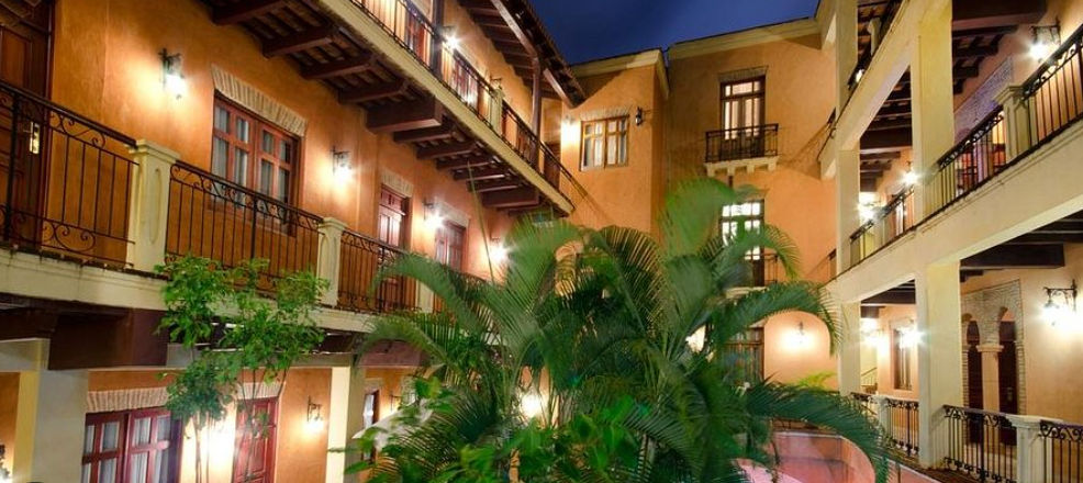 Colonial courtyard of the Boutique Hotel Palacio illuminated at night with tropical plants and wooden balconies.