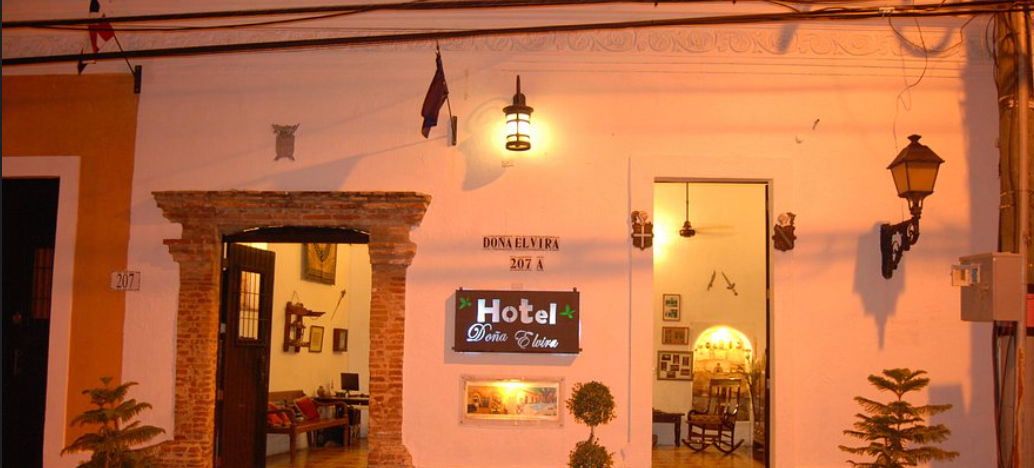 Fachada iluminada del Hotel Doña Elvira en la Zona Colonial de Santo Domingo, mostrando la entrada de estilo colonial con arco de ladrillo y el letrero principal por la noche.