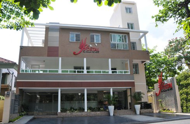 Facade of Hostal San Francisco de Asis in Santo Domingo featuring its distinct red sign, main entrance, and balconies.