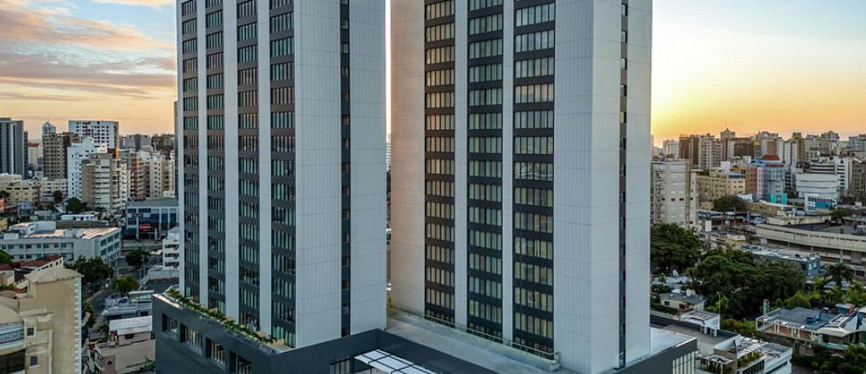 Exterior view of the modern Aloft Santo Domingo Piantini hotel towers standing out against the city skyline at sunset
