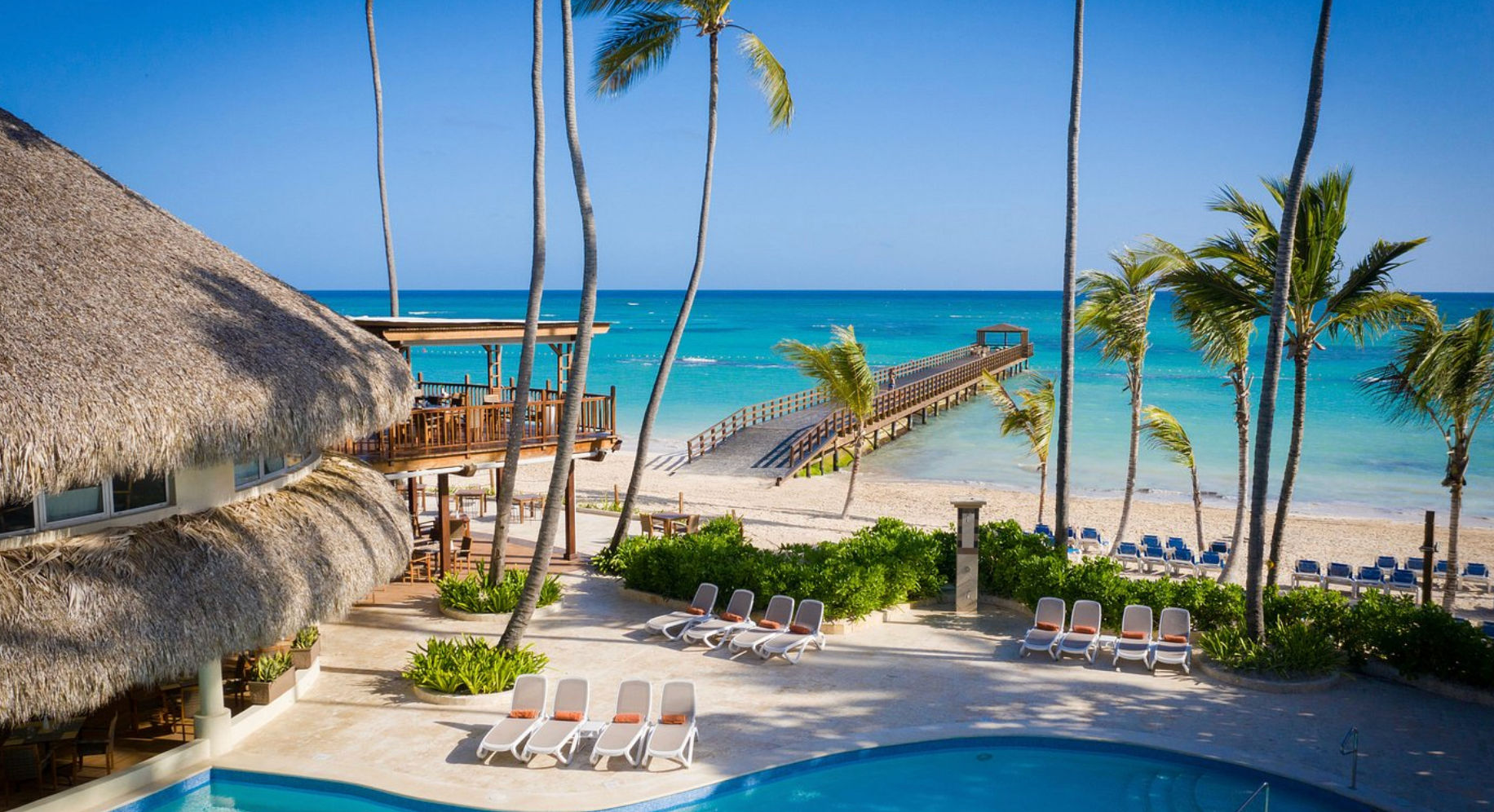 Vista de la piscina, playa y muelle de madera en el hotel Impressive Punta Cana sobre el mar Caribe.
