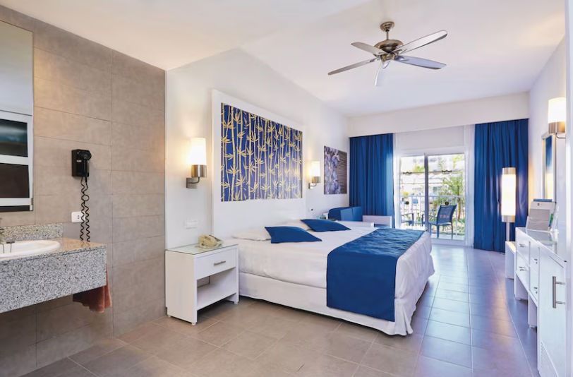Family hotel room at Riu Bambu featuring contemporary tropical decor, comfortable beds, and a balcony overlooking the gardens